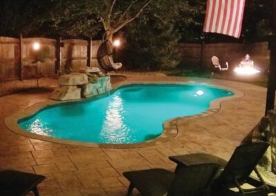Slightly curved edges of inground fiberglass pool at night with stone waterfall and sitting areas on edges