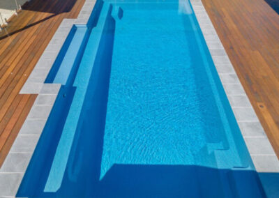 Rectangle inground fiberglass pool with wood deck in sunny date and glass railing