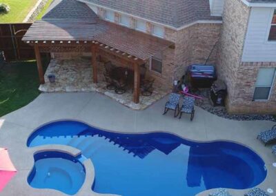 Large curved edge inground fiberglass pool with stairs and sitting areas along edge with attached spa