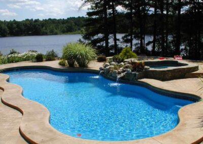 Wavy edged inground fiberglass pool with stone waterfall and hot tub area.