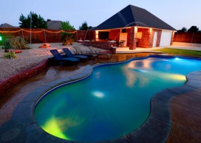 Wavy inground fiberglass pool at night with nights and loungers