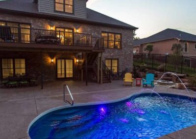 Inground fiberglass pool behind house at night with lights